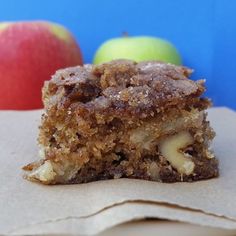 a piece of cake sitting on top of a brown paper bag next to an apple