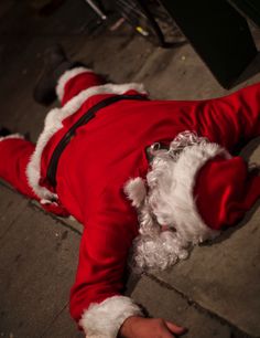 a man dressed as santa claus is laying on the ground with his head down and hands in his pockets