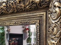 an ornate gold framed mirror in front of a fireplace with christmas decorations on the mantle