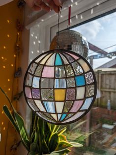 a hand is holding a stained glass ball ornament in front of a window