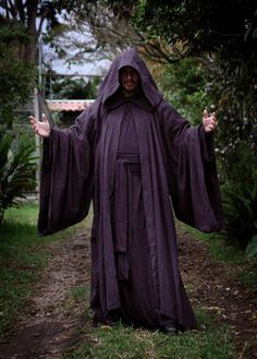 a man dressed in a purple robe and holding his arms out with both hands while standing on a path