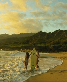 two women are walking into the ocean with their surfboard in hand and one woman is holding her surfboard