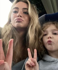 a woman and child making the peace sign with their fingers in front of them,