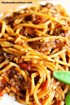 spaghetti with meat and sauce on a white plate next to green leafy garnish