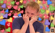 a man with his hands on his face in front of many heart shaped objects behind him