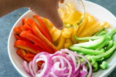 a person pouring dressing into a bowl filled with sliced onions, peppers and carrots