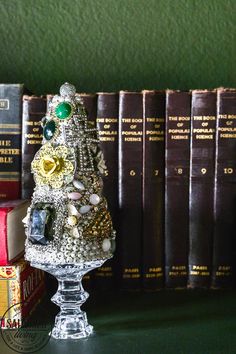 a small christmas tree made out of beads and jewels on a glass stand in front of some books