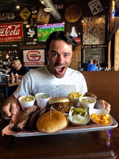 a man holding a tray full of food in front of him with his mouth wide open