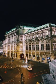 an old building is lit up at night with people walking and riding bikes on the street