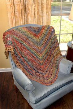 a blue chair with a crocheted blanket on it in front of a window