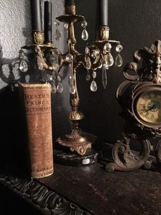 an old fashioned clock sitting on top of a table next to a candle holder and book