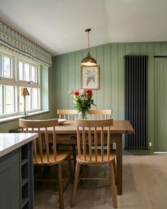 a dining room table with chairs and a vase of flowers on top of it in front of a radiator