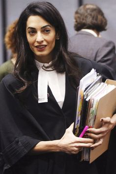 a woman in a court gown holding files and folders while smiling at the camera