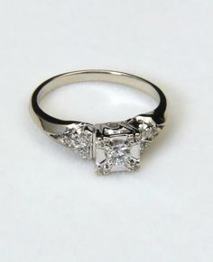 an engagement ring with three stones on the side and two diamonds in the middle, sitting on a white surface