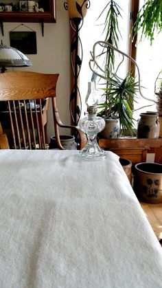 a dining room table with white linen on it and potted plants in the background