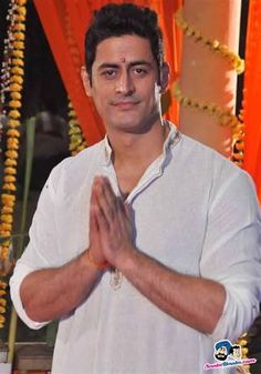 a man standing in front of an orange curtain with his hands folded up and smiling