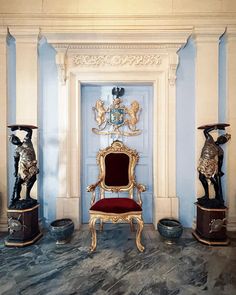 an ornate chair and two statues in front of a blue door