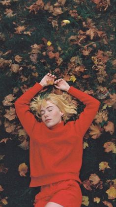 a woman laying on the ground with her hands behind her head, wearing a red sweater and shorts