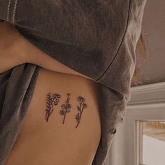 a woman's back with three small flowers on her left side ribcage