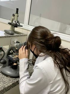 a woman in a lab coat is looking through a microscope at something on the counter