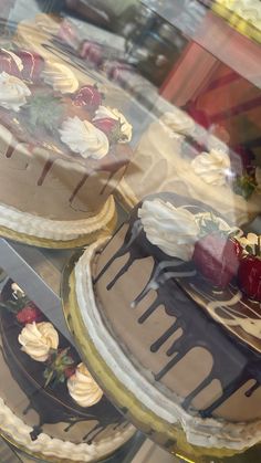 three cakes are on display in a glass case with frosting and strawberries behind them