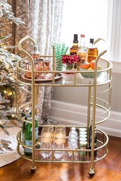 a gold bar cart with drinks on it in front of a christmas tree and window