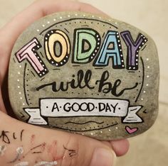 a hand holding a rock with the words today will be a good day written on it