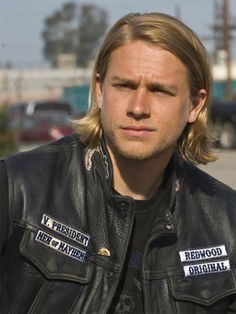 a man with long hair wearing a leather jacket and patches on his chest is staring at the camera