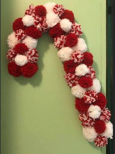 a red and white pom - pom wreath hangs on the wall next to a green door