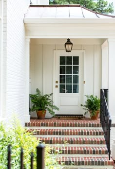 a white front door with two potted plants on the steps