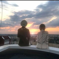 two people standing on top of a building looking at the sunset