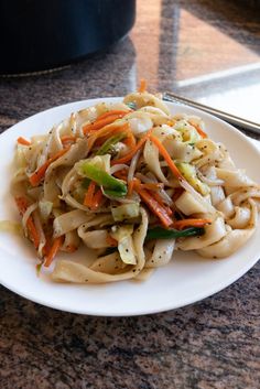 a white plate topped with noodles and veggies next to a pot of broccoli