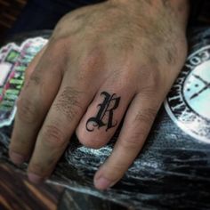 a person with a small tattoo on their ring finger and the letter k in black ink