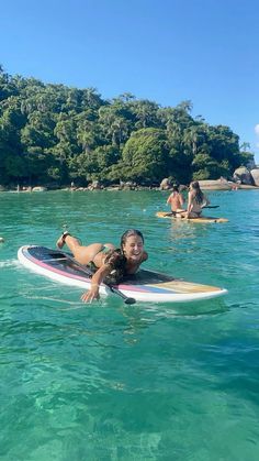 a woman is laying on a surfboard in the water with other people swimming nearby