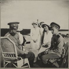 an old black and white photo of four people sitting on chairs in front of the water