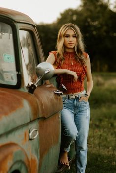 a woman standing next to an old rusted truck with her hand on the door handle