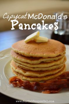 a stack of pancakes with bacon and butter sitting on a plate next to a glass of syrup