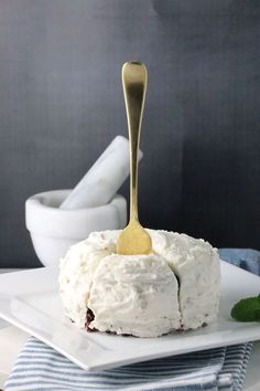 a white plate topped with a cake covered in frosting and a golden spoon sticking out of it