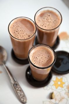 three glasses filled with liquid sitting on top of a table next to two spoons