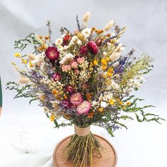 a vase filled with lots of colorful flowers on top of a wooden stand next to a white wall