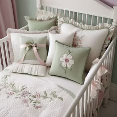 a white bed topped with lots of pillows covered in pink and green flowers next to a window