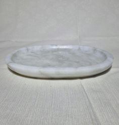 a white marble plate sitting on top of a white tablecloth covered floor next to a wall