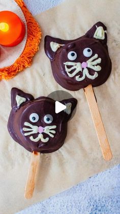 two chocolate cats on sticks with candles in the background and an orange candle next to them