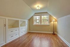 an empty room with wooden floors and white cabinets in the corner is lit by a lamp