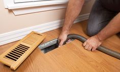 a man kneeling on the floor with a vacuum in front of him and a grate next to it