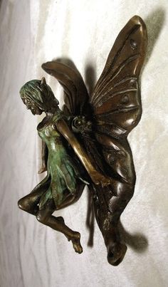 a bronze fairy figurine sitting on top of a white sheet next to a wall