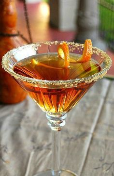 an alcoholic drink with orange peels in a martini glass on a table next to a bottle