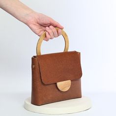 ✨ Crafted from genuine vegetable-tanned leather, this elegant shoulder purse emits a timeless charm. Adding a touch of sophistication to any outfit, its rich chestnut hue is complemented by a versatile design that seamlessly blends style with functionality. This purse boasts an inner synthetic felt lining with a convenient pocket for keeping your essentials organized. The magnetic snap closure ensures secure storage, while the detachable and adjustable crossbody strap allows for effortless customization, with a length of up to 115 cm (59 inches) and a width of 2 cm (0.7 inches). Whether worn as a crossbody bag for hands-free convenience or carried as a chic clutch, this accessory seamlessly transitions from day to night. For added versatility, it also includes a wooden handle for easy carr Small Leather Bag, Shoulder Purse, Vegetable Tanned Leather, Wooden Handles, Leather Handbag, Crossbody Strap, Leather Purses, Cross Body Handbags, Purses And Handbags