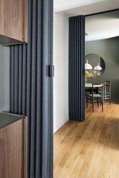 an open door leading to a dining room with wooden floors and black curtains on the windows