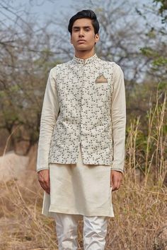 White bundi with zardozi, resham, cutdana embroidery in floral pattern. Paired with textured stripe pattern kurta and churidar. - Aza Fashions Fitted Nehru Jacket With Cutdana For Festivals, Fitted Chanderi Nehru Jacket For Festivals, Fitted Chanderi Nehru Jacket For Designer Wear, Cutdana Nehru Jacket For Festivals, Designer Chanderi Nehru Jacket Fitted, White Nehru Jacket With Dabka Embroidery, Fitted Nehru Jacket With Dori Work For Navratri, Transitional Nehru Jacket With Dori Work, Transitional Dori Work Nehru Jacket